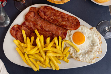 There is freshly cooked breakfast on plate - scrambled eggs with pieces of fried potatoes and dried pork meet bacon. Traditional European Spanish breakfast is fried eggs with bacon.
