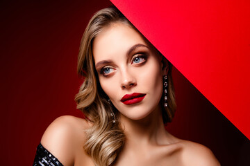 Charming blonde woman in shimmering black dress with red lipstick against a bold red backdrop