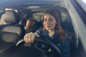 Woman driving car with child in backseat on a sunny day