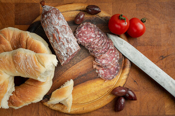 A rustic feast: Salami, sausage, bread, tomatoes, and olives arranged on a wooden board, capturing the simple pleasures of a shared meal and culinary delights.