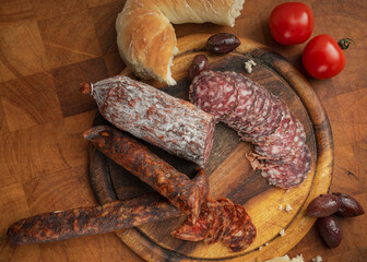 A rustic feast: Salami, sausage, bread, tomatoes, and olives arranged on a wooden board, capturing the simple pleasures of a shared meal and culinary delights.