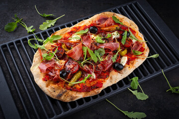 Traditional Italian pinsa bread prosciutto e salsa di pomodoro with Parma ham, buffalo mozzarella tomato sauce served as close-up on an old rustic grill grid