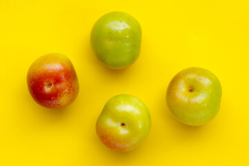Fresh green plum fruit on yellow background.