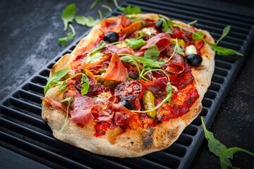 Traditional Italian pinsa bread prosciutto e salsa di pomodoro with Parma ham, buffalo mozzarella tomato sauce served as close-up on an old rustic grill grid