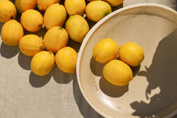 Multiple lemons spread across a surface with three placed in a plate,