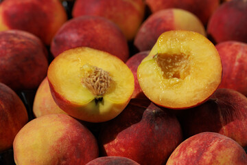 A close-up of fresh peaches, one cut in half, with the juicy, bright flesh inside