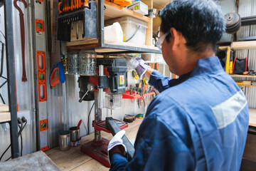 Latin technician using a drill press on a metal component in a workshop