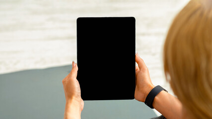 Home workout with devices. Adult woman with fitness tracker and tablet with blank screen sits on mat, on floor, close up, copy space