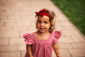 Close up. Summer portrait of smiling baby girl in a red dress, with a red bow on her head.