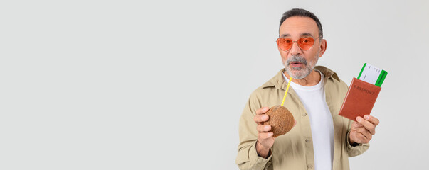 Joyful senior man in funky sunglasses sips from a coconut while holding a passport and boarding...