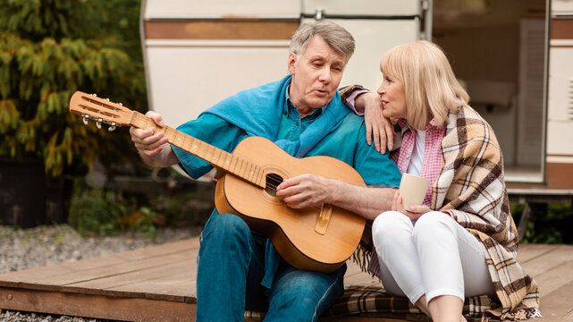 Retired couple with acoustic guitar singing together near their motorhome at campsite