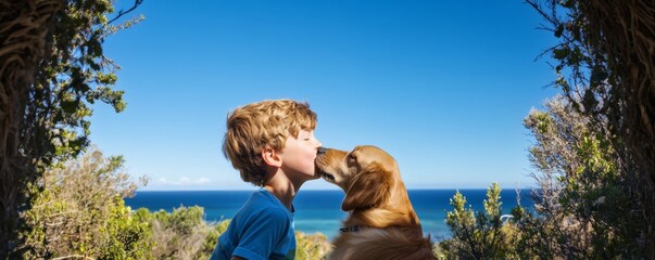 Fototapeta premium A young boy kisses his golden dog near the ocean