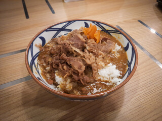 A bowl of Japanese curry rice dish with sliced beef topping served on a wooden patterned table. 
