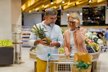 Senior couple choosing pineapple in supermarket fruit and vegetable section