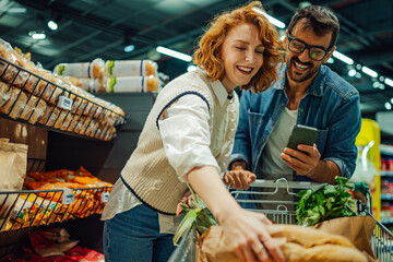 Happy couple using smartphone and choosing products in supermarket