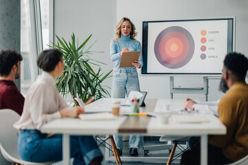 Young businesswoman leading a meeting using a digital whiteboard, presenting data to her colleagues