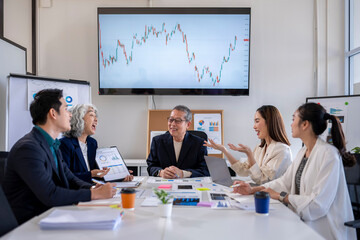 A group of people are sitting around a table with a large screen behind them