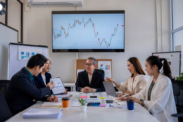 A group of people are sitting around a table with a large monitor behind them