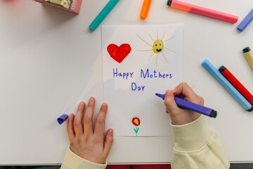 Child drawing happy mothers day card with colorful markers