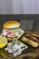 Lobster salad sandwich on a brioche bun with coleslaw, sliced lemon, and fried yuca