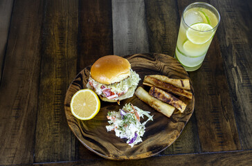 Lobster salad sandwich on a brioche bun with coleslaw, sliced lemon, and fried yuca