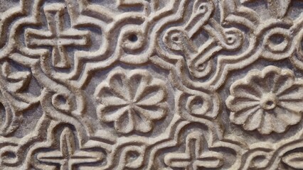 Venice, Italy - December 28, 2024: A close-up of an intricately carved stone surface featuring symmetrical floral and cross motifs interconnected by looping patterns.