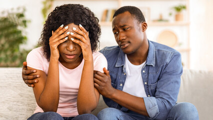 Relationships problems. Black guy comforting his crying girlfriend, home interior, closeup