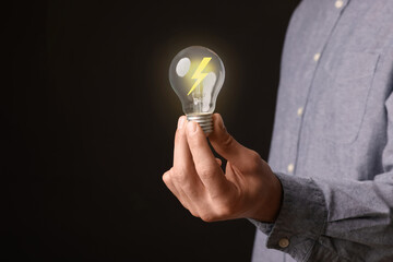 Man holding light bulb with lightning inside on black background, closeup. Concepts of idea,...