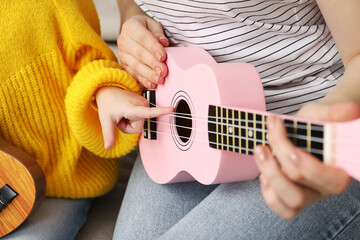 Woman teaching little girl to play ukulele at home, closeup