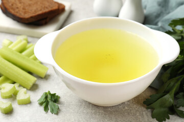 Tasty chicken bouillon in bowl, celery and parsley on grey table, closeup