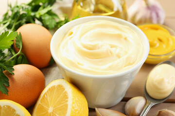 Delicious mayonnaise sauce in bowl and ingredients on table, closeup