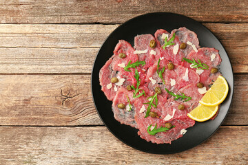 Delicious beef carpaccio with arugula, capers, cheese and lemon on wooden table, top view. Space for text