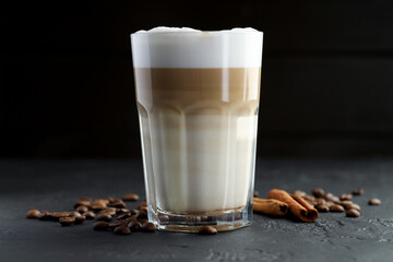 Tasty latte macchiato in glass, coffee beans and cinnamon on black table, closeup