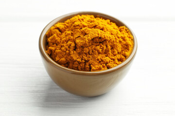 Turmeric powder in bowl on white wooden table, closeup
