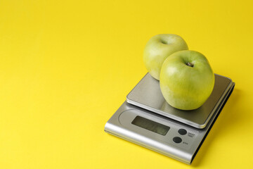 Electronic kitchen scale with apples on yellow background, closeup. Space for text