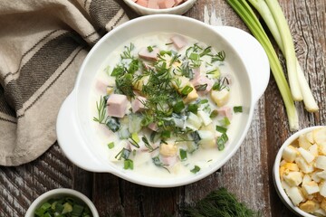 Delicious okroshka soup in bowl and ingredients on wooden table, flat lay