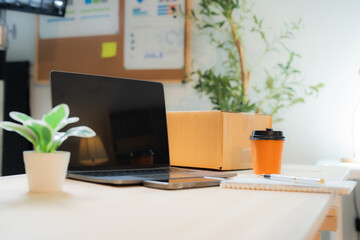 Cozy home office desk featuring laptop, cardboard box, coffee cup, notebook and pen, embodying the essence of online business and remote work
