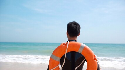 Obraz premium Man in a rescue uniform, standing near the shoreline with the sea behind him. For blogs on emergency preparedness, public safety, working as a lifeguard