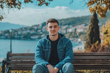 A young man sits outdoors looking calmly towards the viewer