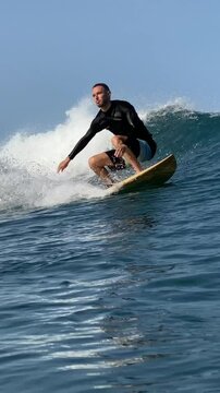 Vertical video of a young man surfing in the clear waters of the Indian Ocean on a sunny day.Bali island.Indonesia