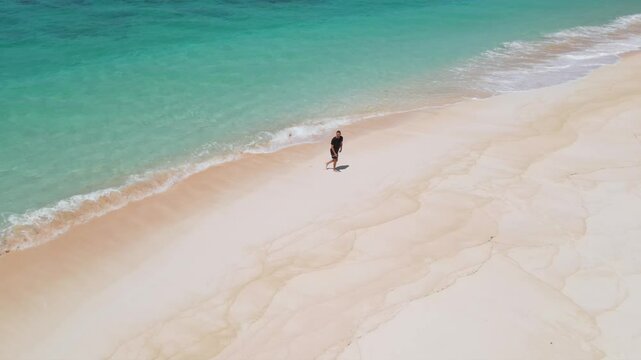 Young man walking on a tropical beach on a sunny day.Indonesia.Aerial view