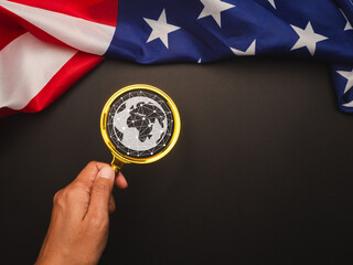Hand holding a magnifying glass with a futuristic globe, placed against the American flag.