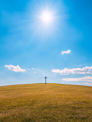 Obraz premium A serene landscape features a solitary cross on a grassy hill under a brilliant sunlit sky, symbolizing hope, faith, and tranquility in nature's embrace.