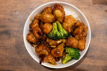 Overhead shot of savory fried chicken in tangy sauce with green broccoli florets on a wooden table. Perfect for lunch or dinner, a classic.
