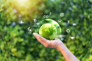 Businessman holding green grass globe with eco-friendly icons, symbolizing sustainability.