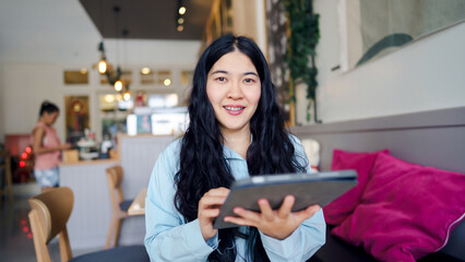 Business woman consultant motivation concept. A woman with long hair smiles while using a tablet in a cozy cafe setting.
