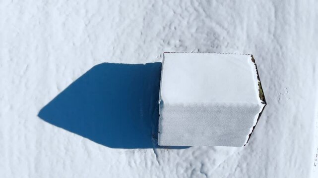 Aerial: zenital shot of a snowy cabin in the Alps in a sunny day