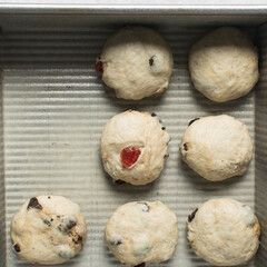 Overhead view of hot cross bun dough rising in a silver baking pan, top view of bun dough rolled into balls in a baking tin, process of making hot cross buns