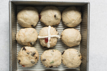 Overhead view of cross being piped on hot cross bun dough in a silver baking pan, process of making hot cross buns