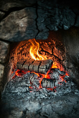 Close-up of a rustic burning fireplace with glowing embers and flames in a stone setting, creating a warm, cozy atmosphere.